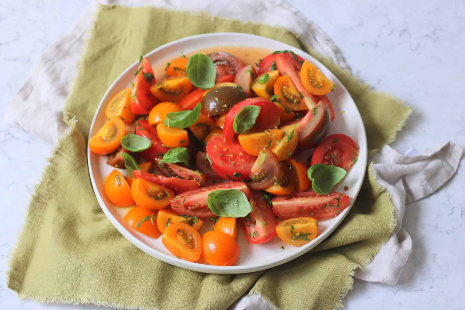 A Gremolata Topped Tomato Salad served on a white platter on top of a green napkin.