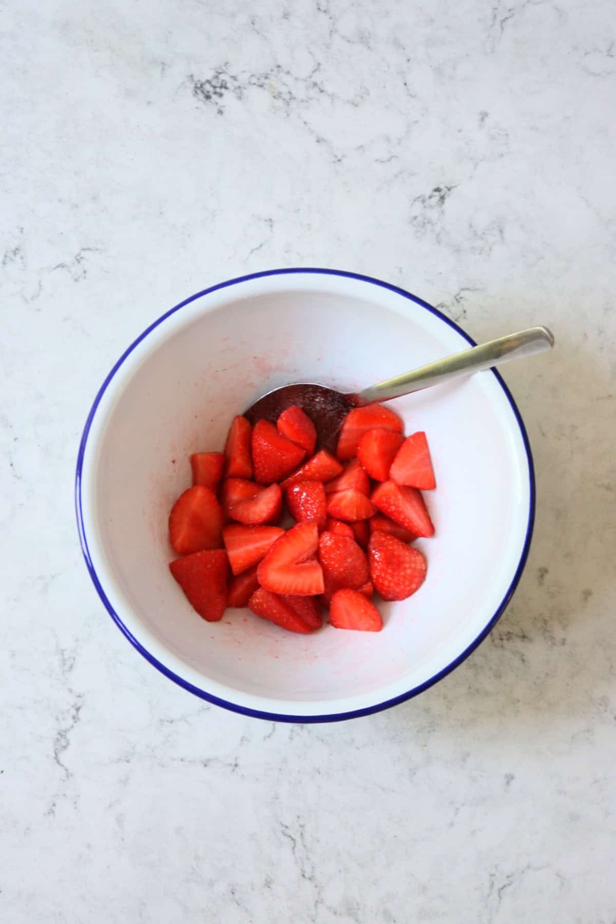 Strawberries in a white and blue enamel bowl macerating with caster sugar