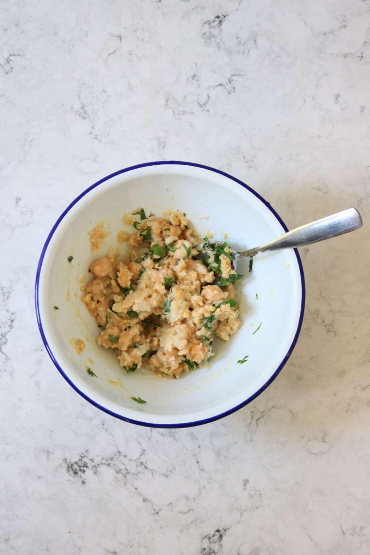 Mashed chickpeas, yogurt and herbs in a white enamel bowl with a metal spoon
