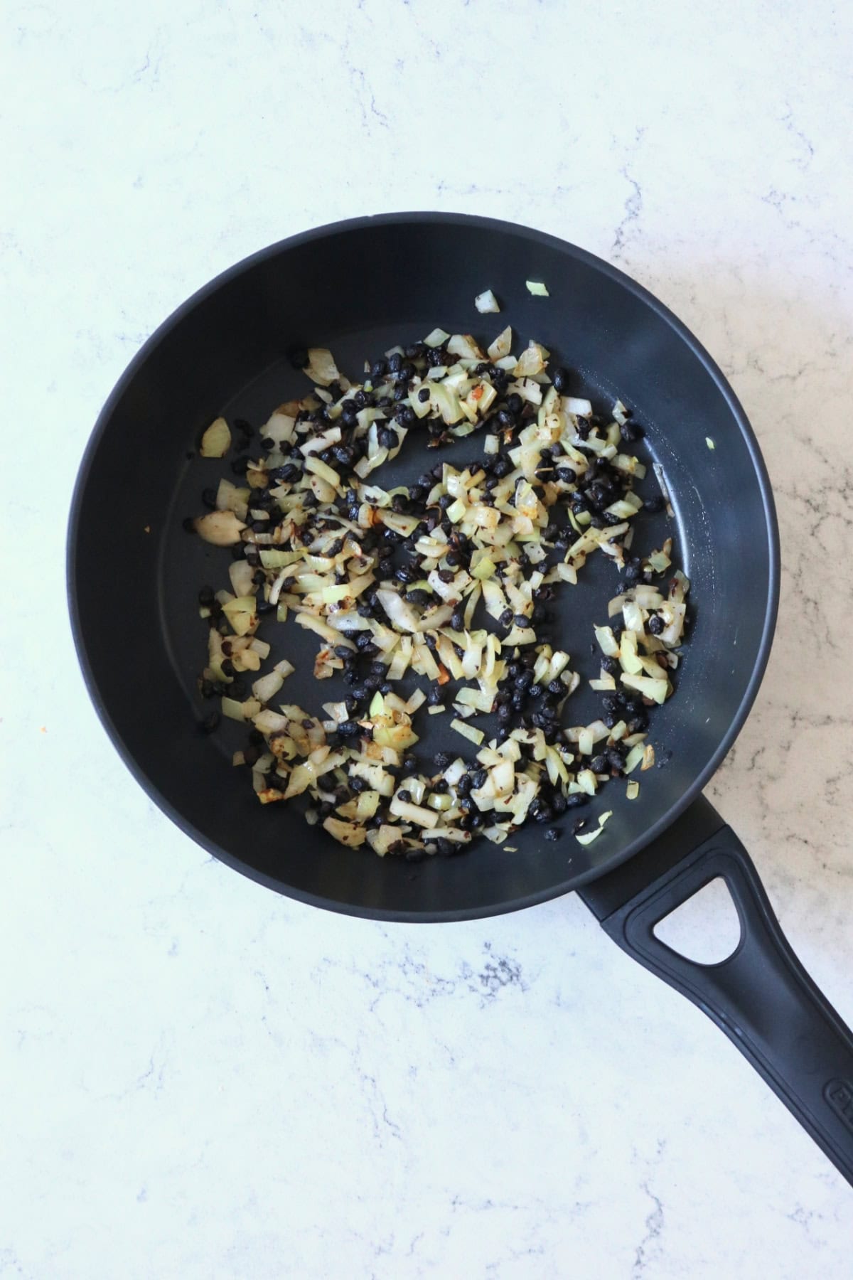 Onions and fermented black beans frying in a large flat bottomed frying pan