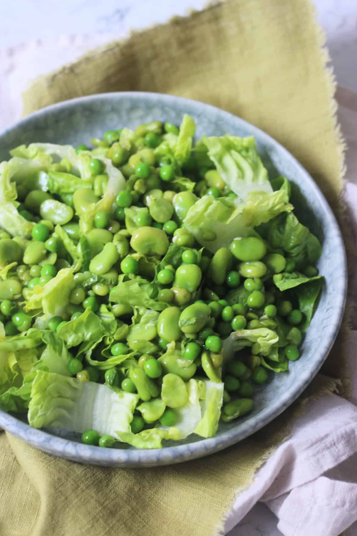 Pea and Broad Bean Salad with Little Gem Lettuce and Fresh Mint dressed with Dijon Mustard Dressing served on a light blue plate on top of a green napkin.