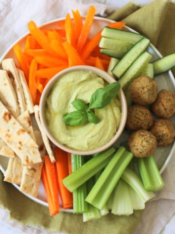 A crudites platter made up of pitta, carrots, celery, falafel, cucumber and orange pepper with a bowl of Roasted Garlic and Basil Hummus