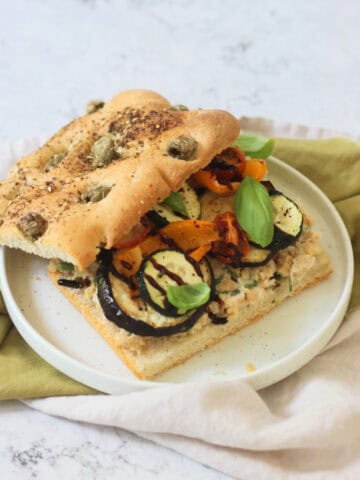 A Roasted Vegetable and Chickpea Focaccia Sandwich with the top slice of bread slightly askew showing the filling underneath