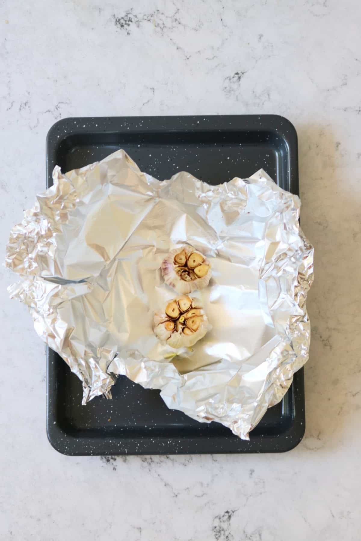 2 heads of roasted garlic in tin foil on a baking tray