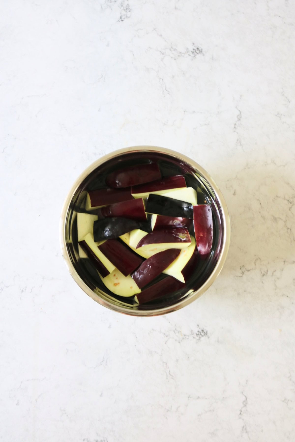Wedges of aubergine in a bowl of salty water