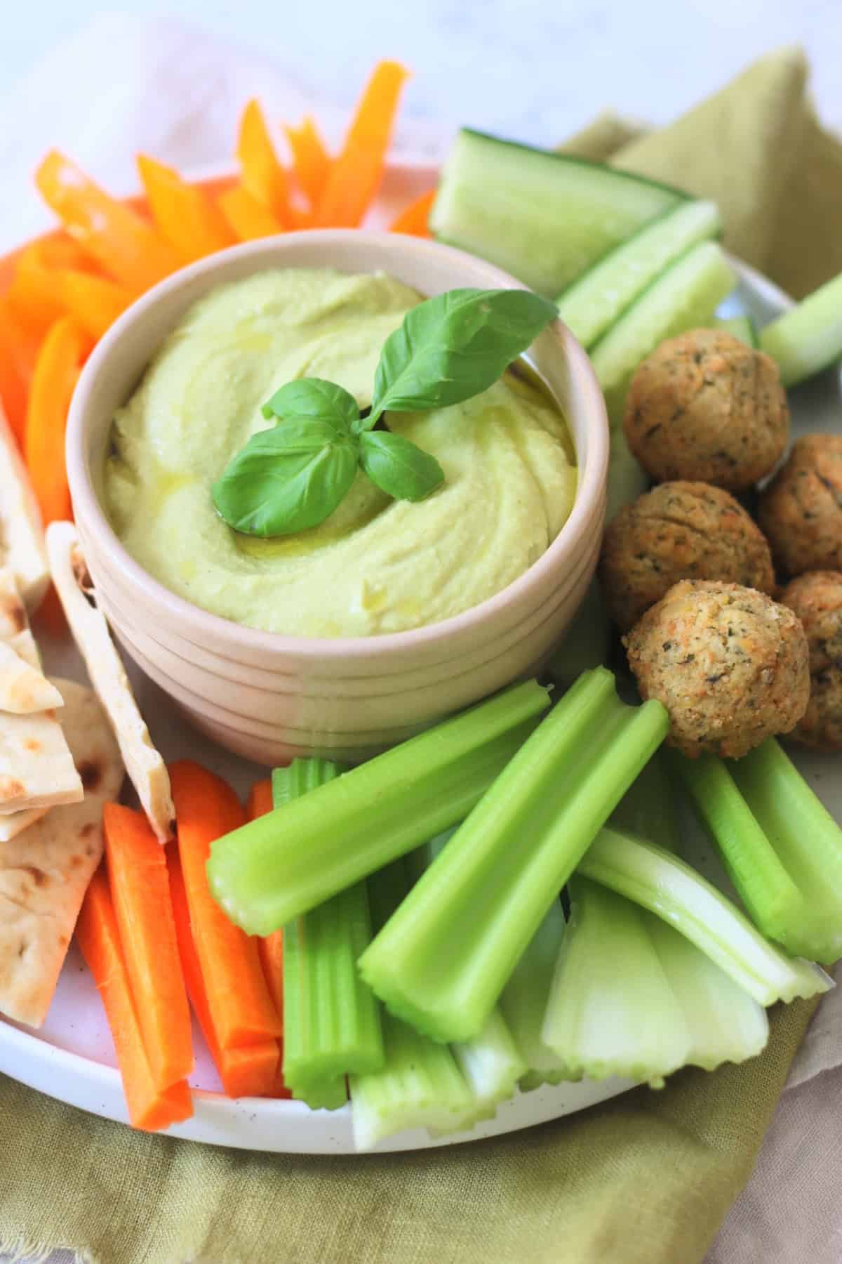 A crudites platter made up of pitta, carrots, celery, falafel, cucumber and orange pepper with a bowl of Roasted Garlic and Basil Hummus