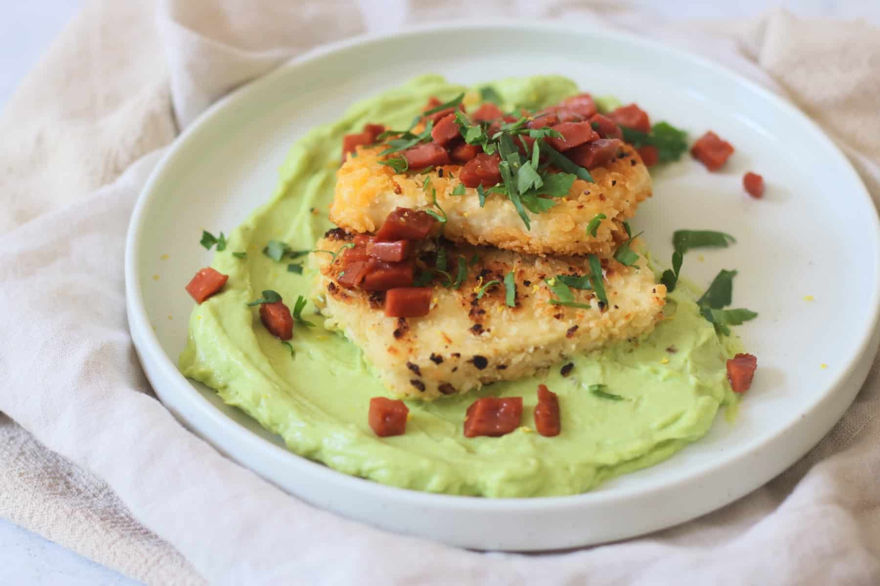 A plate of Crispy Lemon Pepper Tofu with Creamy Avocado Sauce and Bacon Crunch with fresh parsley.