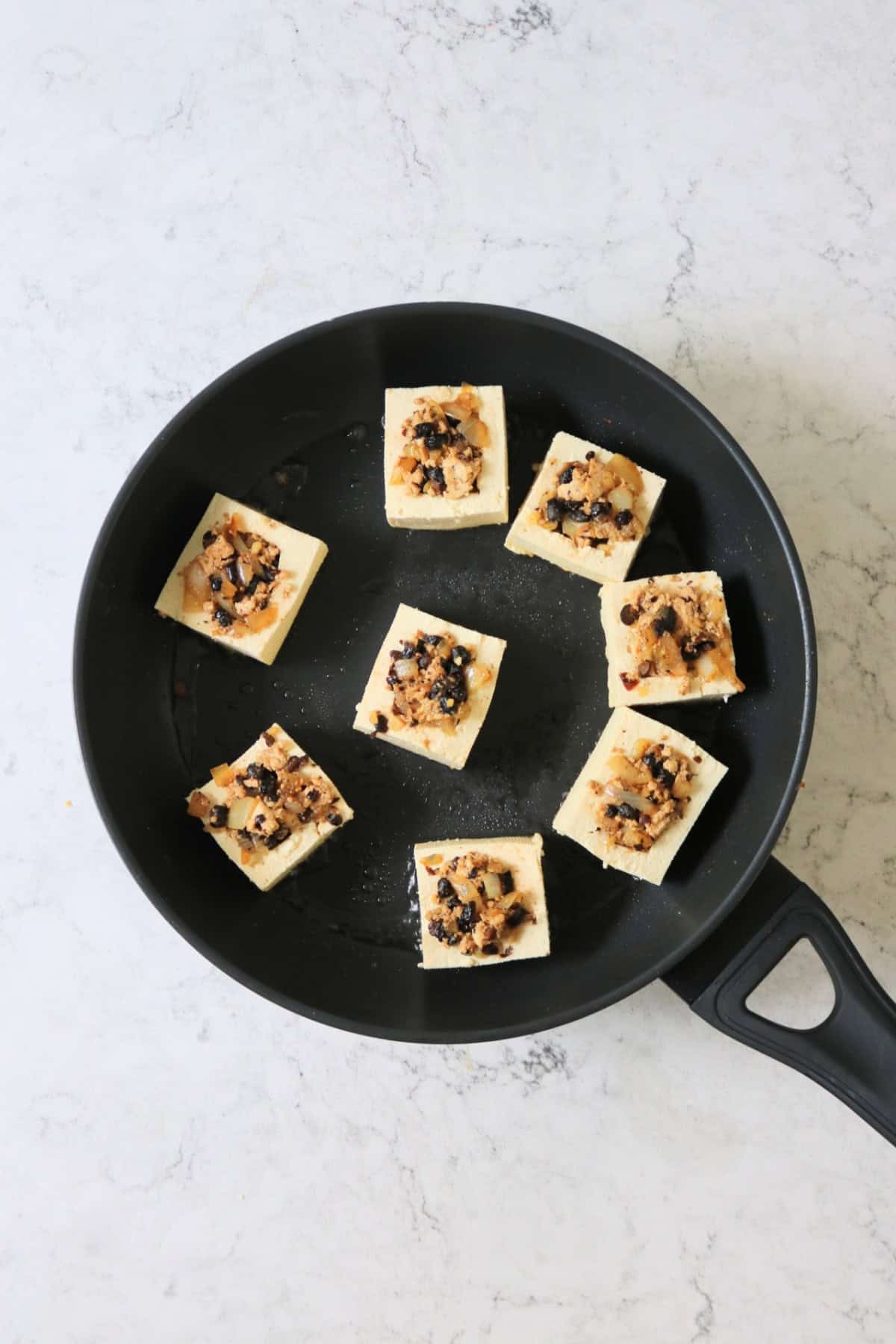 Tofu stuffed with black beans being fried in a large frying pan