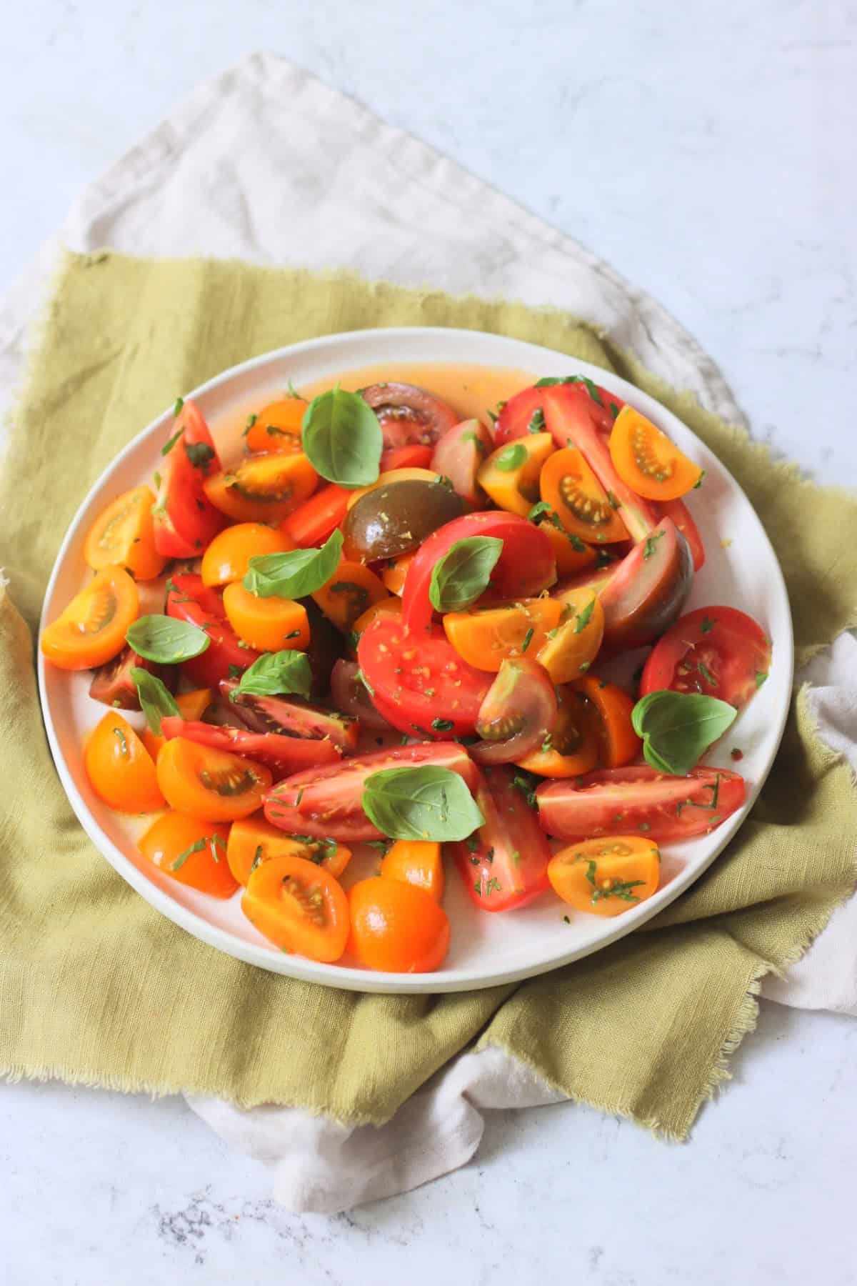 A Gremolata Topped Tomato Salad served on a white platter on top of a green napkin.