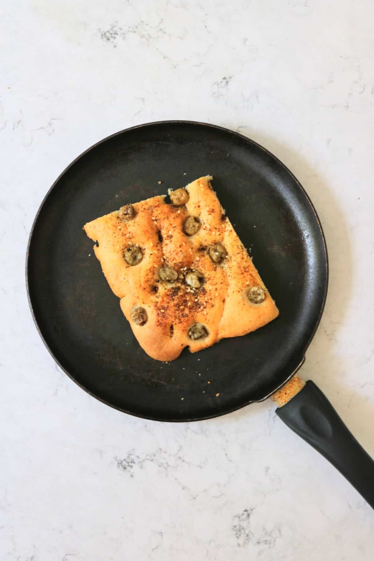 A square of focaccia being toasted in a dry frying pan