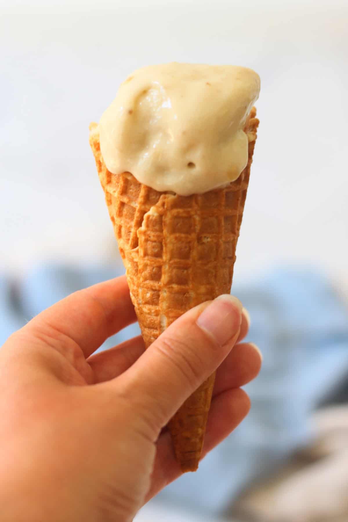A hand holding a waffle cone of Vegan Banana and Coconut Ice Cream