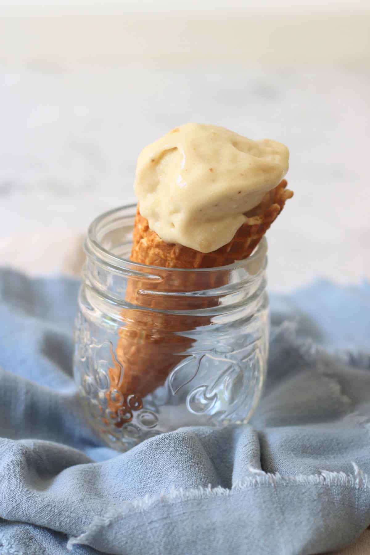A waffle ice cream cone topped with Vegan Banana and Coconut Ice Cream resting in a glass jar