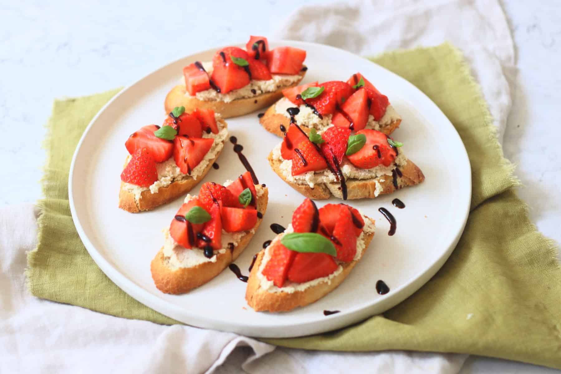 6 Vegan Ricotta and Strawberry Crostini served on a white plate on top of a green napkin.