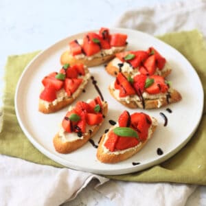 6 Vegan Ricotta and Strawberry Crostini served on a white plate on top of a green napkin.