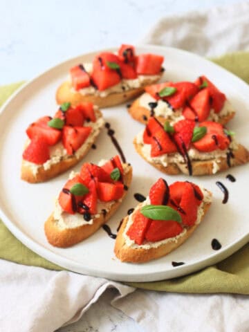 6 Vegan Ricotta and Strawberry Crostini served on a white plate on top of a green napkin.