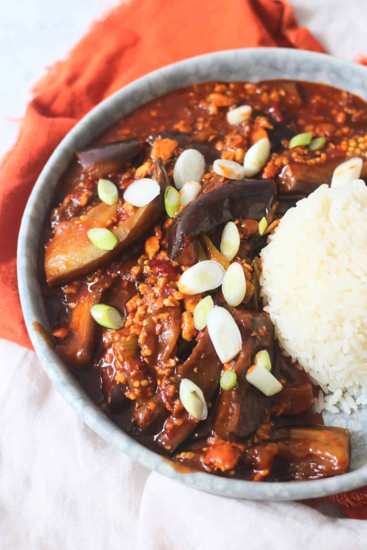 Vegan Sichuan Style Braised Aubergines topped with sliced spring onions and served with white rice