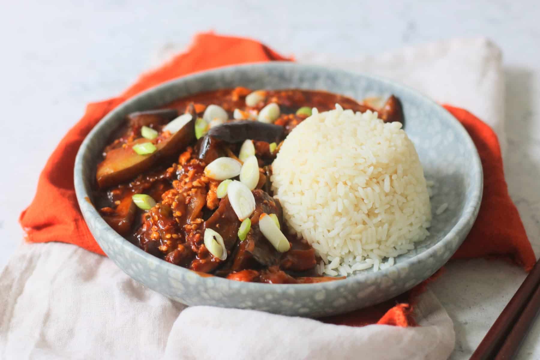 Vegan Sichuan Style Braised Aubergines topped with sliced spring onions and served with white rice