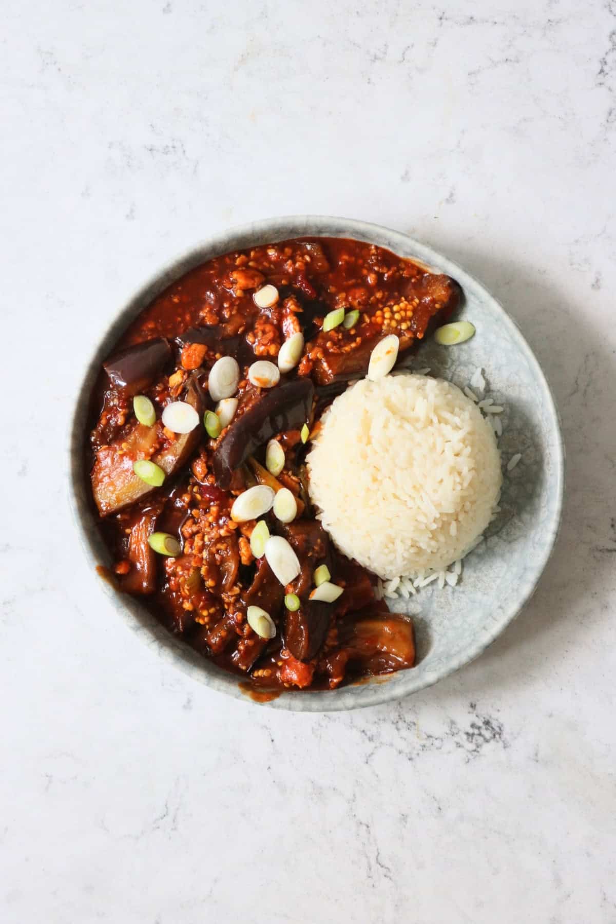 Vegan Sichuan Style Braised Aubergines topped with sliced spring onions and served with white rice