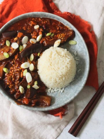 Vegan Sichuan Style Braised Aubergines topped with sliced spring onions and served with white rice
