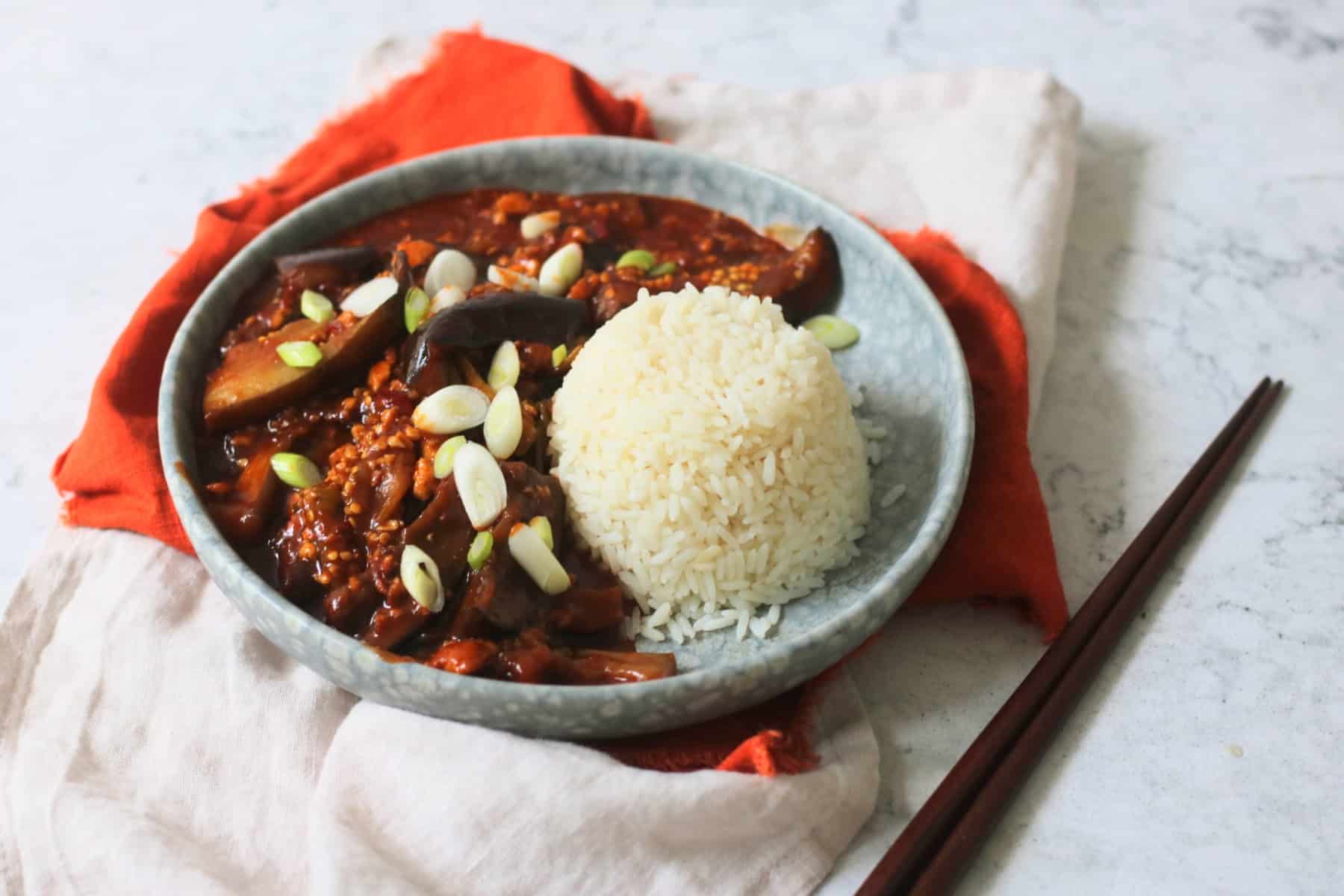 Vegan Sichuan Style Braised Aubergines topped with sliced spring onions and served with white rice
