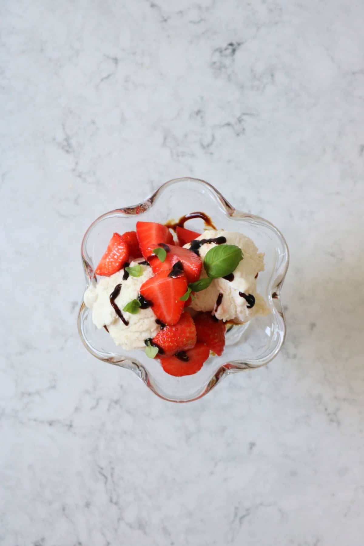 A Vegan Strawberry and Balsamic Ice Cream Sundae made up of layers of balsamic glaze, dairy free ice cream, macerated strawberries and basil leaves served in an ice cream sundae glass.