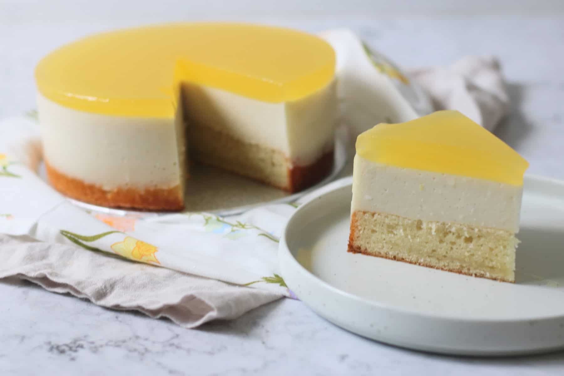 A Vegan White Chocolate and Lemon Mousse Cake with a slice cut out of it, served on a white side plate.