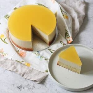 A Vegan White Chocolate and Lemon Mousse Cake with a slice cut out of it, served on a white side plate.