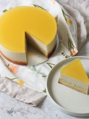 A Vegan White Chocolate and Lemon Mousse Cake with a slice cut out of it, served on a white side plate.