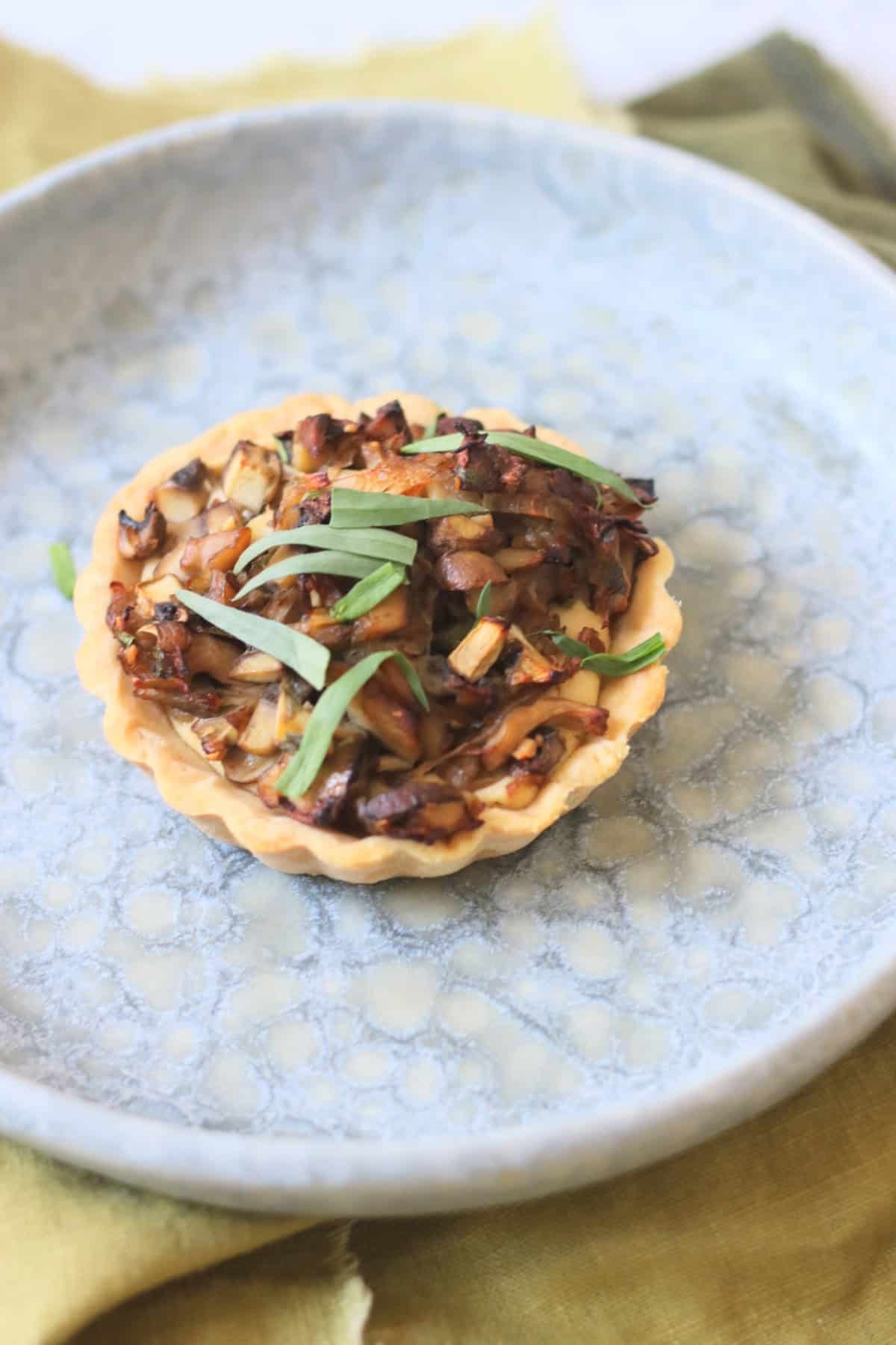 A Vegan Wild Mushroom Tartlet with Caramelised Shallots on a plate with a green napkin