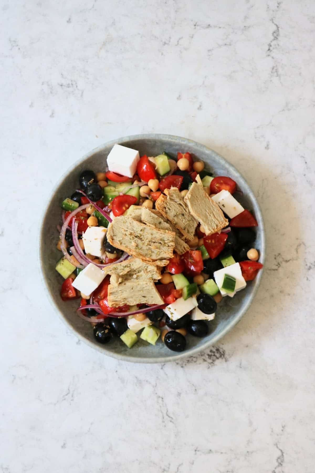 A plate of Greek Inspired Salad with Vegan Chicken Slices.