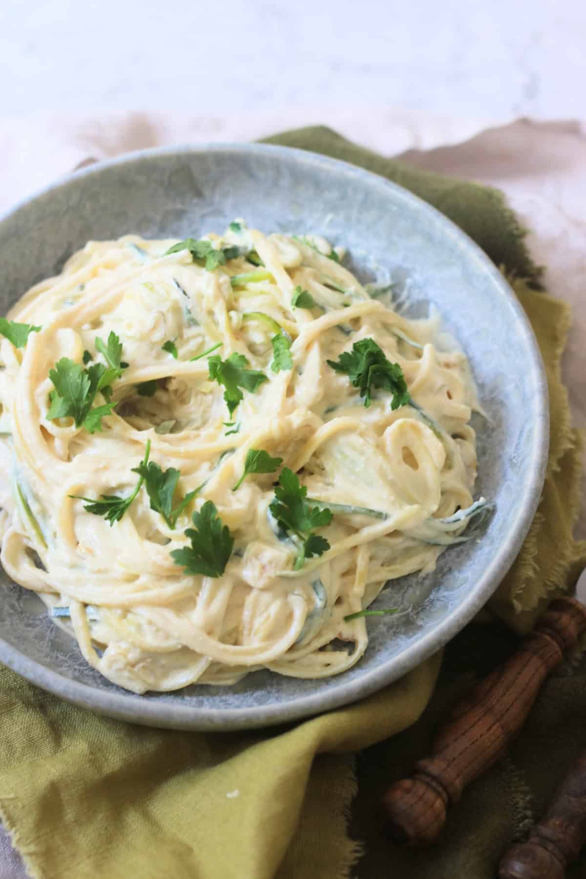 A plate of Vegan Creamy Courgette Linguine topped with fresh parsley served on a blue plate with green napkins and wooden handled knife and fork.