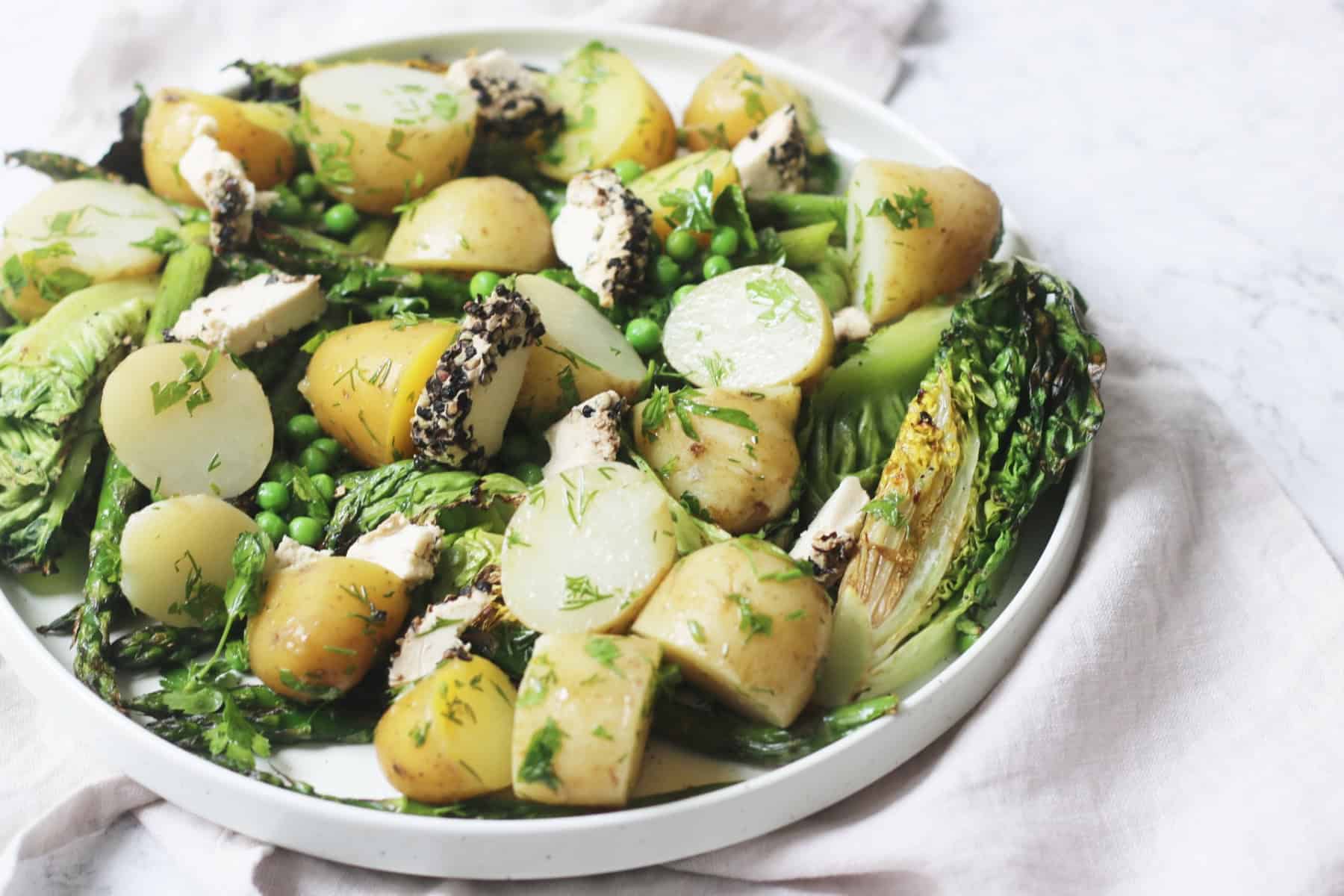 A large plate of BBQ Charred Lettuce Salad with Pepper-Crusted Vegan Goat's Cheese, New Potatoes & Asparagus on a white napkin