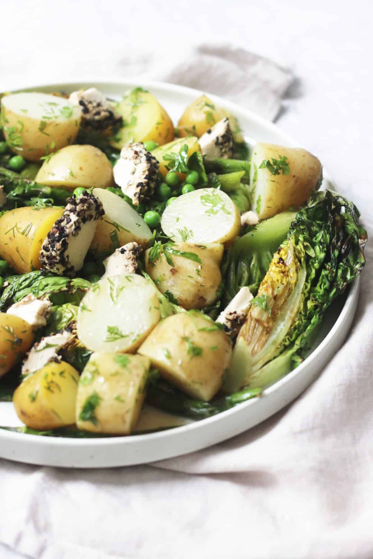 A large plate of BBQ Charred Lettuce Salad with Pepper-Crusted Vegan Goat's Cheese, New Potatoes & Asparagus on a white napkin