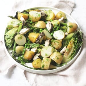A large plate of BBQ Charred Lettuce Salad with Pepper-Crusted Vegan Goat's Cheese, New Potatoes & Asparagus on a white napkin