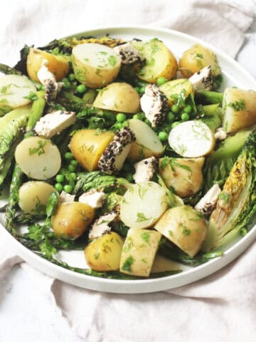 A large plate of BBQ Charred Lettuce Salad with Pepper-Crusted Vegan Goat's Cheese, New Potatoes & Asparagus on a white napkin