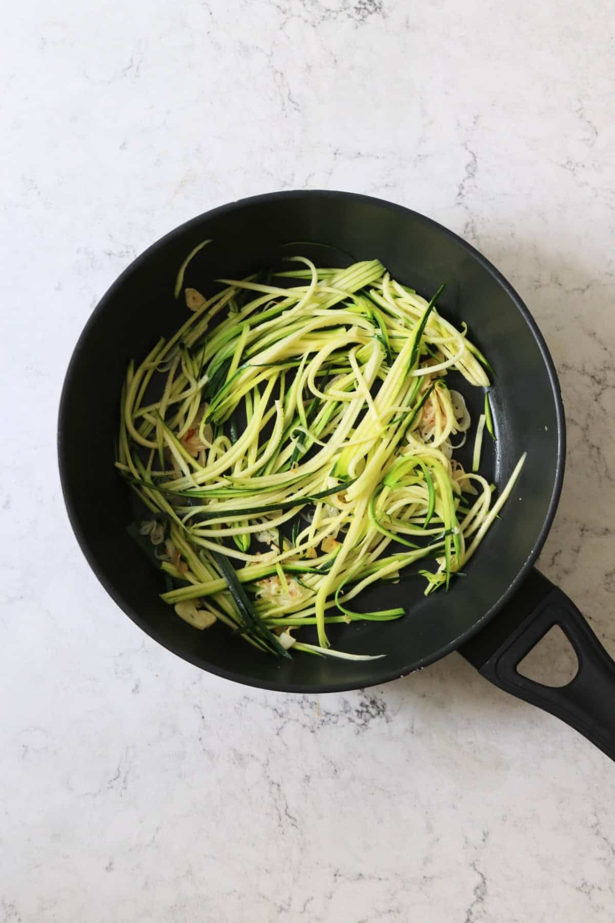 Ribbons of courgette frying in a large pan with shallots and garlic
