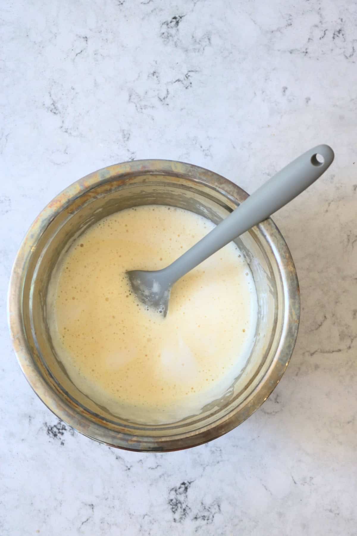 An egg-free quiche filling in a mixing bowl with a grey spatula