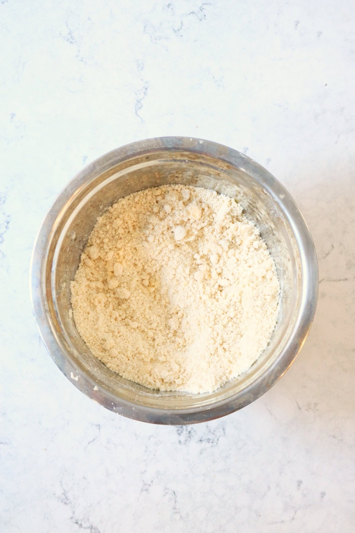 Vegan butter and flour rubbed together to form a breadcrumb like texture in a metal mixing bowl