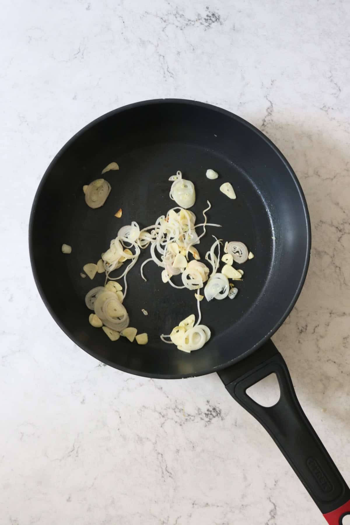 Thinly sliced shallots and garlic frying in a large flat bottomed frying pan