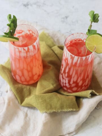 Two tall glasses of Watermelon Agua Fresca garnished with lime wheels and mint served on a green napkin