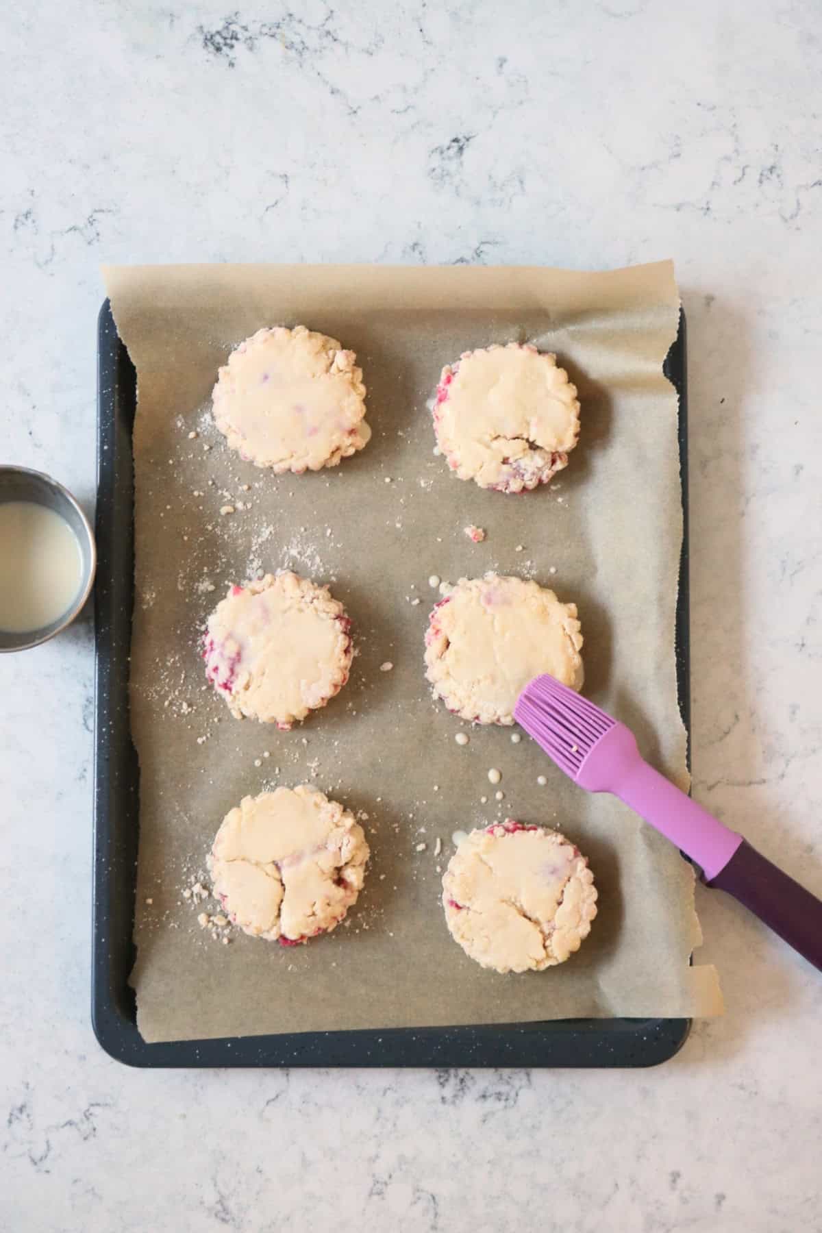 Glazing Vegan Raspberry and Lemon Scones with plant milk using a pink and purple silicone pastry brush