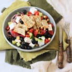 A plate of Greek Inspired Salad with Vegan Chicken Slices sat on green napkins with wooden handled knife and fork.