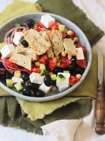 A plate of Greek Inspired Salad with Vegan Chicken Slices sat on green napkins with wooden handled knife and fork.