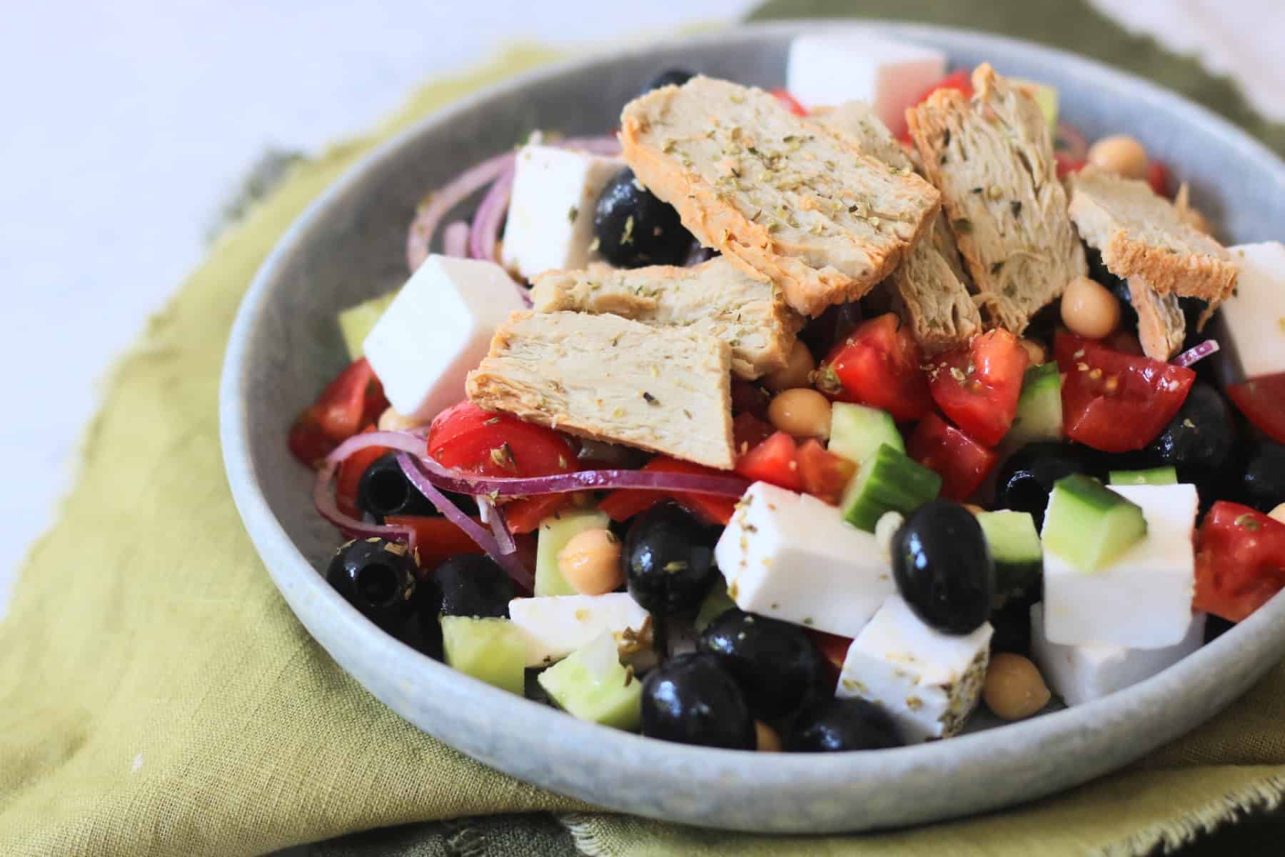 A plate of Greek Inspired Salad with Vegan Chicken Slices sat on green napkins
