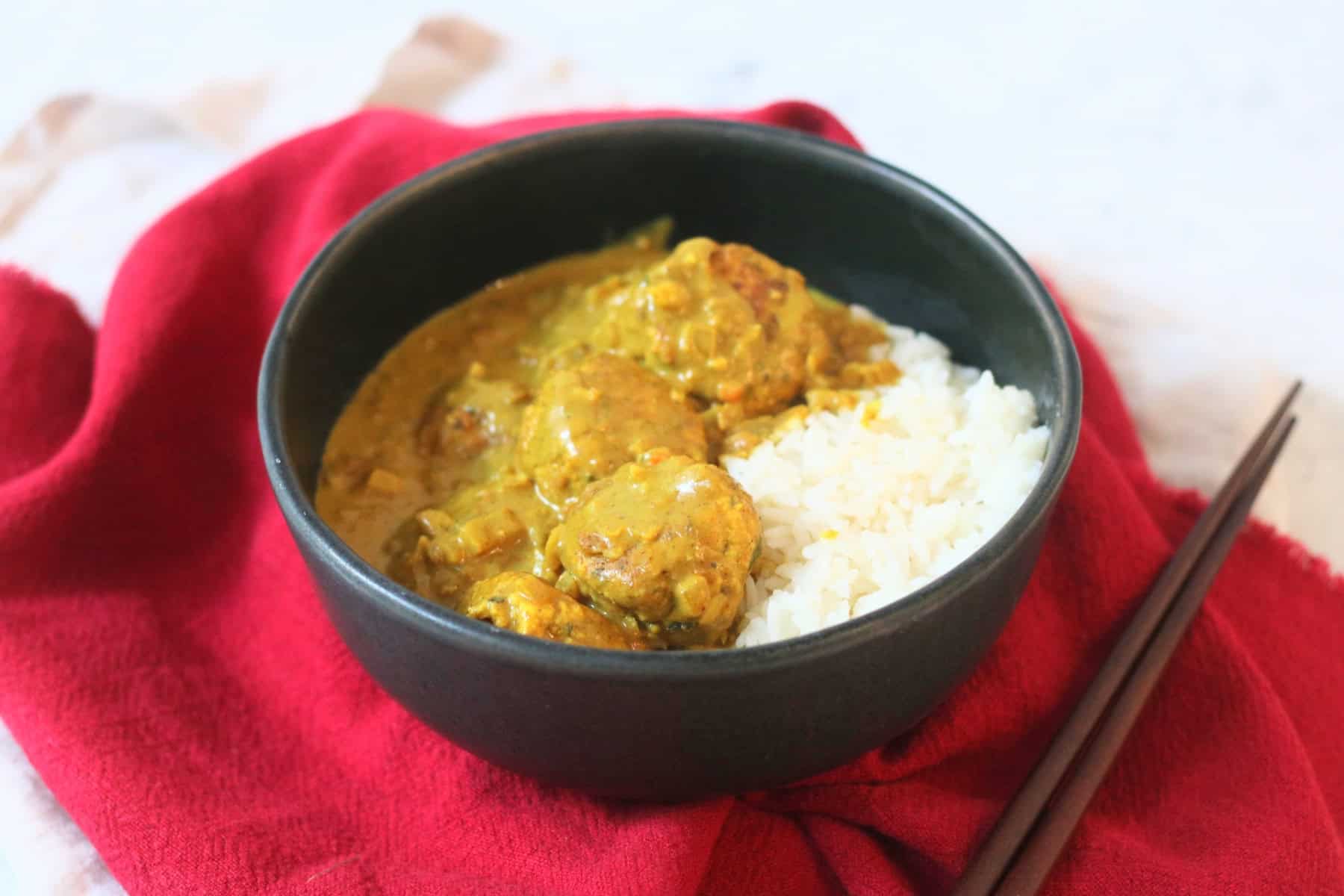 Hong Kong Style Vegan Curry Fish Balls served with white rice in a black bowl with a red napkin and wooden chopsticks