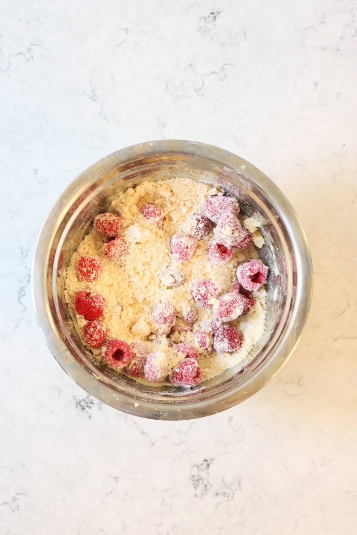Mixing raspberries into the dry ingredients of scone dough in a metal mixing bowl