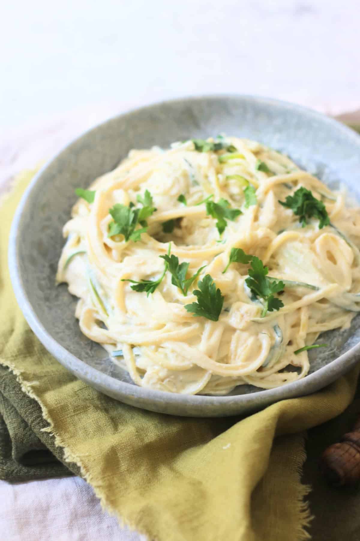 A plate of Vegan Creamy Courgette Linguine served on a blue plate with green napkins.