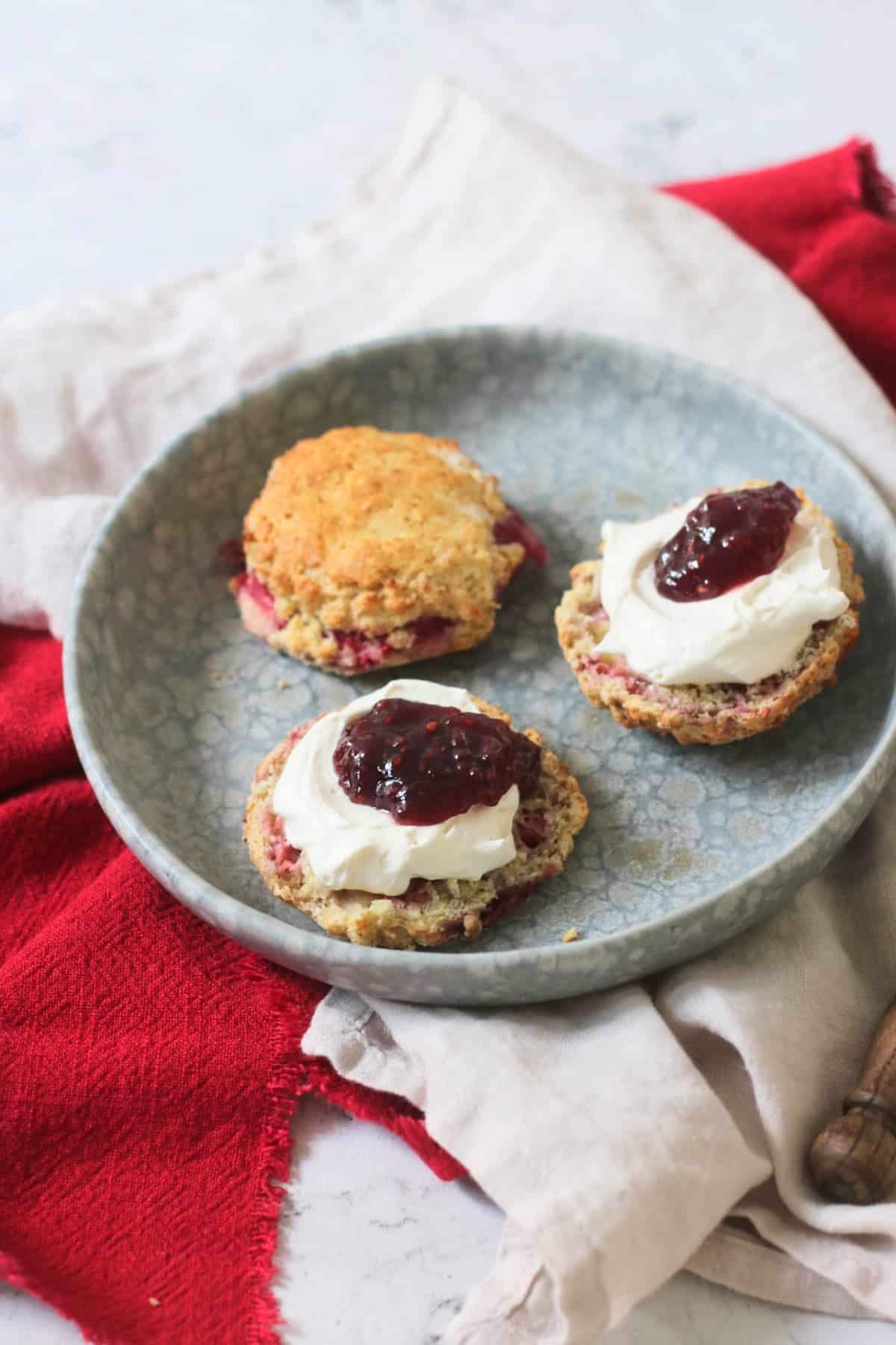 Vegan Raspberry and Lemon Scones on a plate topped with vegan cream and raspberry jam