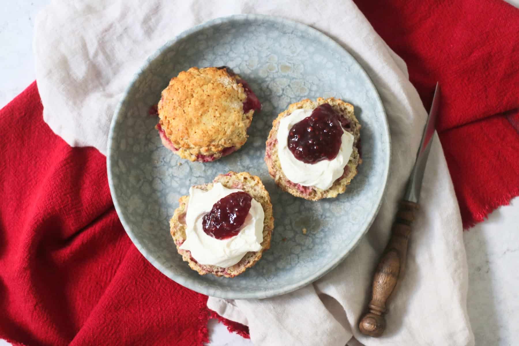 Vegan Raspberry and Lemon Scones on a plate topped with vegan cream and raspberry jam