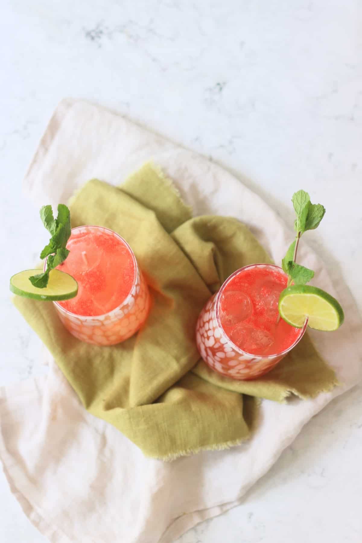 Two tall glasses of Watermelon Agua Fresca garnished with lime wheels and mint served on a green napkin